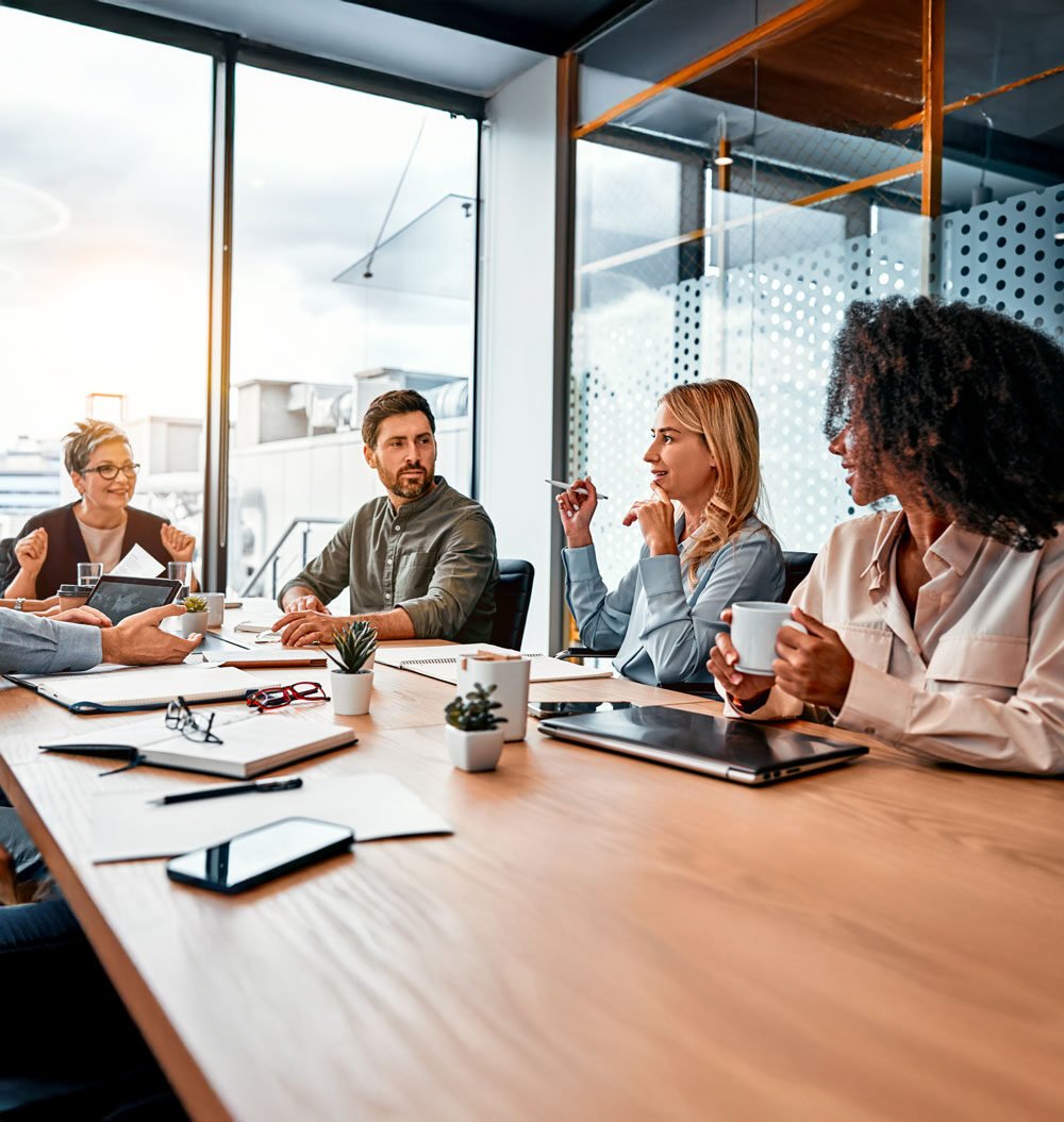 A diverse group of team members are meeting in the office, having a discussion around the table.